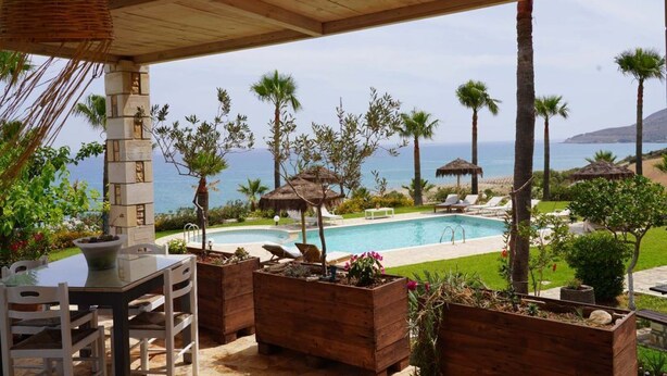 A covered outdoor area with a pool, wooden planters, and lounge chairs. - Aneria Suites (Rethymno)