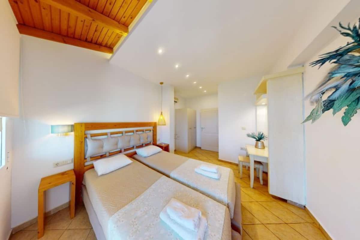 A hotel room with two beds, a wooden headboard, a small table, and a plant.