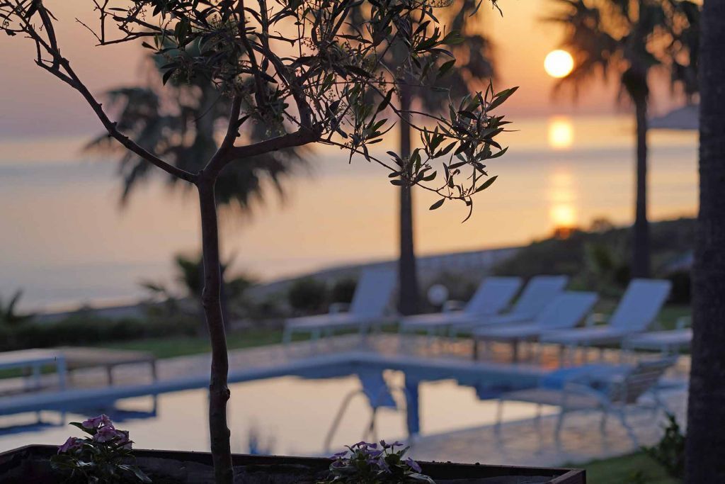 Vista da piscina com espreguiçadeiras e um pôr do sol sobre a água.