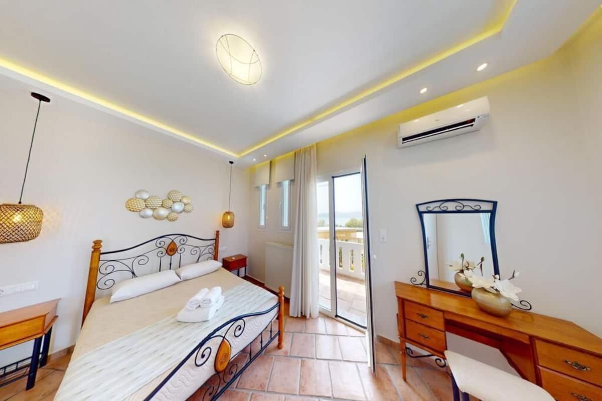 A bedroom with a bed, bedside table, dresser, mirror, and an air conditioning unit.