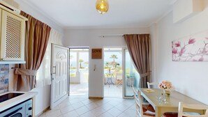 A bright room with a kitchen area, a dining table with chairs, and a view of the outdoors. - Aneria Suites (Rethymno)