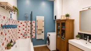 A modern bathroom with a bathtub, a washing machine, and a cabinet with towels.