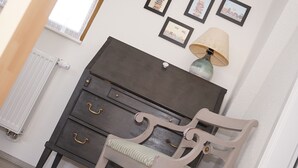 Une pièce avec une commode en bois foncé, une chaise de couleur claire avec un coussin à rayures, une lampe posée sur la commode et des tableaux encadrés accrochés au mur.
