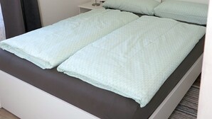 Un lit simple avec une tête de lit blanche, une table de chevet avec une lampe et un tableau encadré au mur.