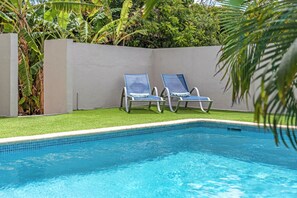 Piscina con dos sillas de descanso y un muro perimetral.
