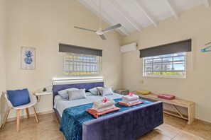 Un dormitorio con cama, una silla, un escritorio y dos ventanas.