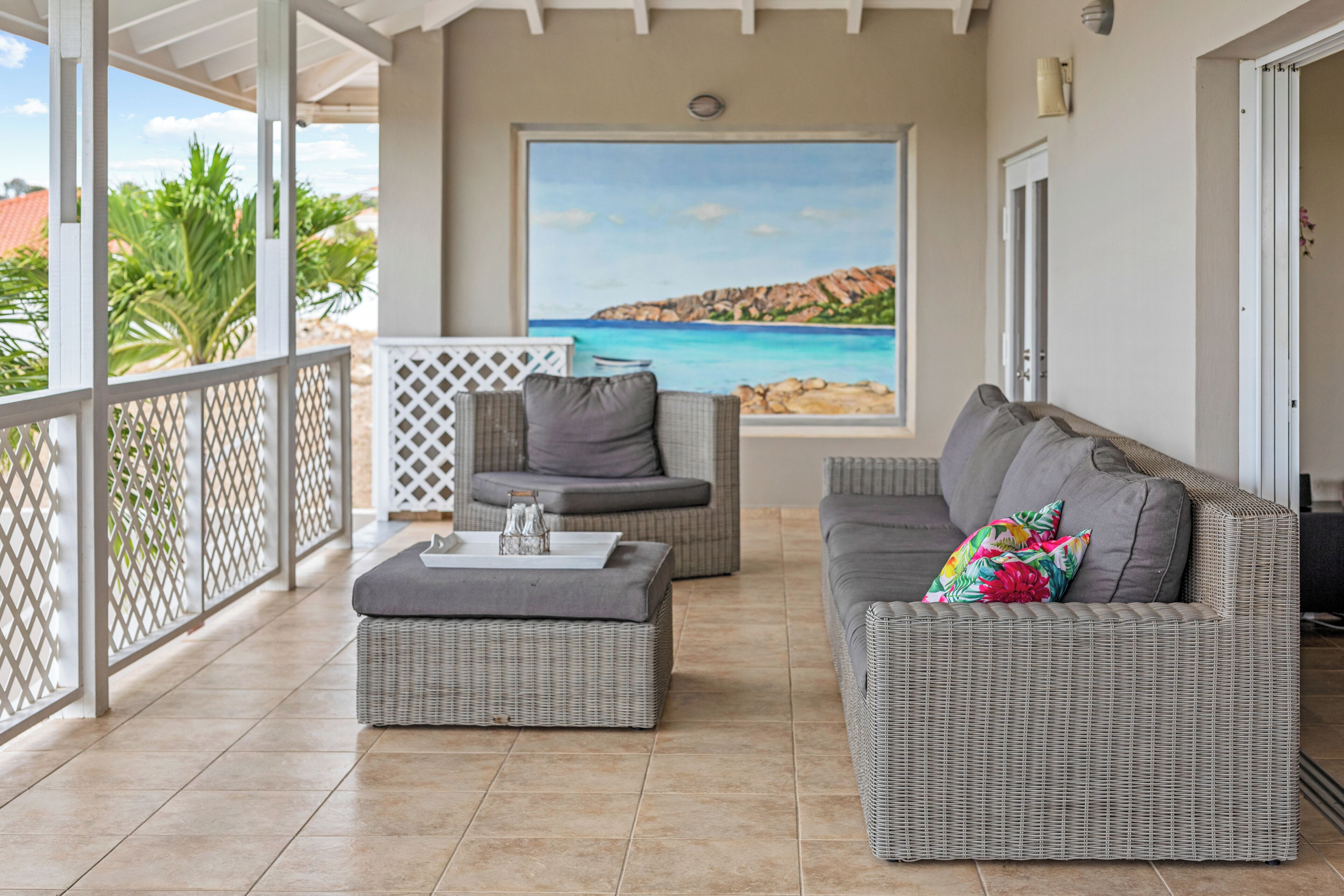 A balcony with wicker furniture, a view of the sea, and a door leading to the interior.