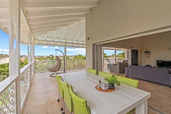 A covered outdoor patio with a dining table, chairs, and a hanging chair.