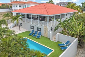 A two-story house with a red roof, a pool, and a covered patio area.