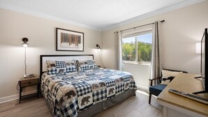 Une chambre à coucher avec un lit, des lampes de chevet, un bureau avec une chaise, une fenêtre avec des rideaux et un tableau encadré au mur.