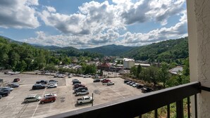 Un parking où sont garés divers véhicules, entouré de collines verdoyantes et avec une ville en arrière-plan.