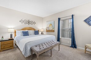 A bedroom with a large bed, bedside tables, a bench, a window with curtains, and wall art.