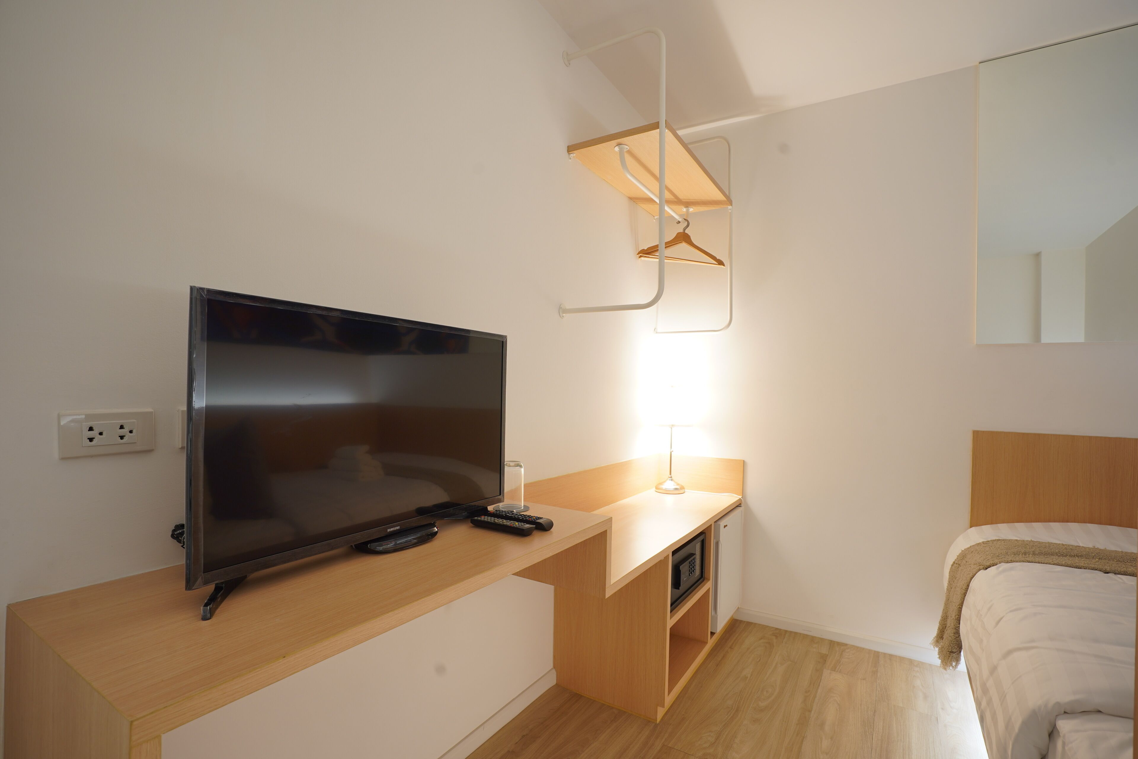 Una habitación de hotel moderna con televisor de pantalla plana, una mesita de noche con lámpara, cabecera de madera y microondas incorporado.