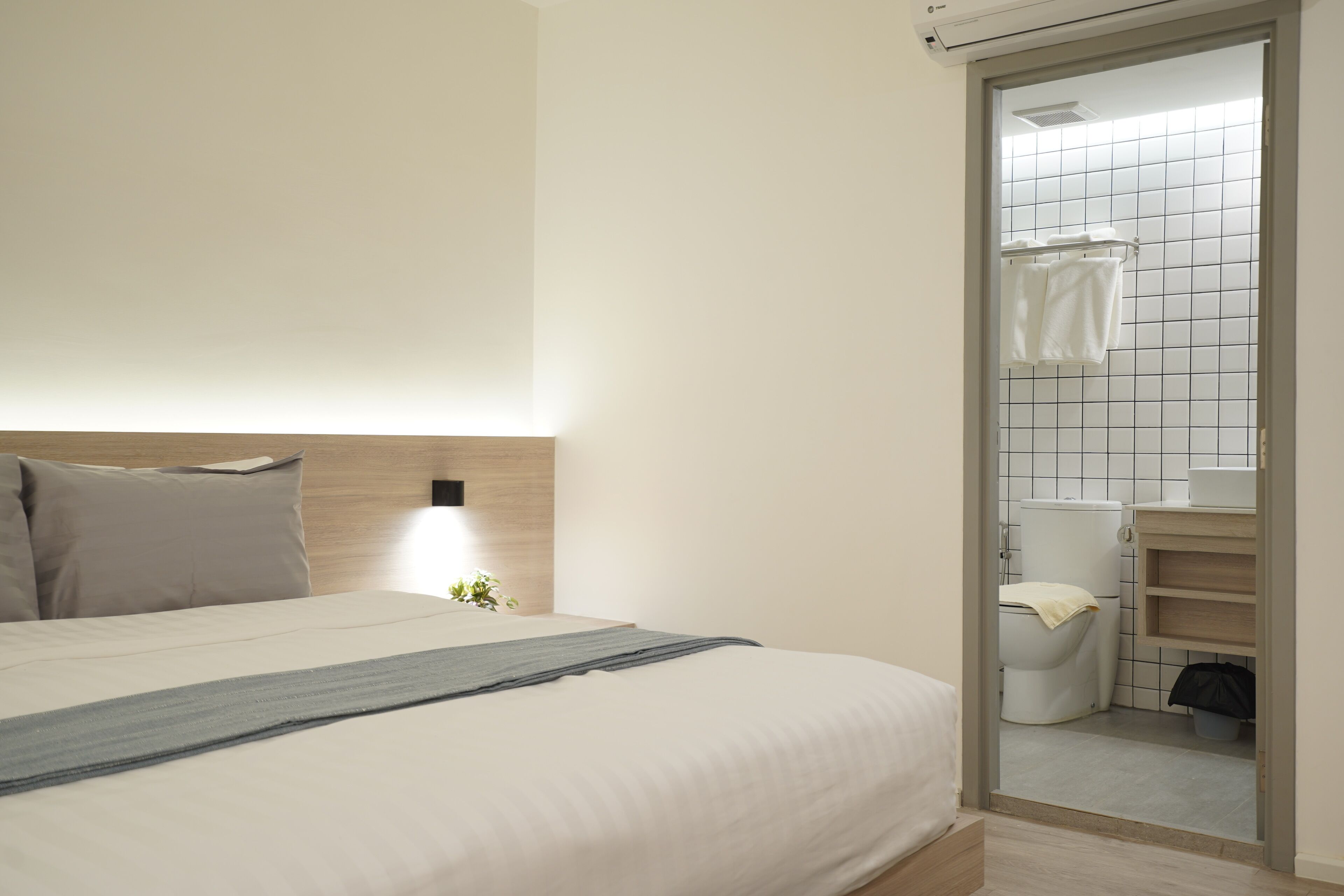 A bedroom with a bed, bedside table, and a view into the bathroom through an open door.