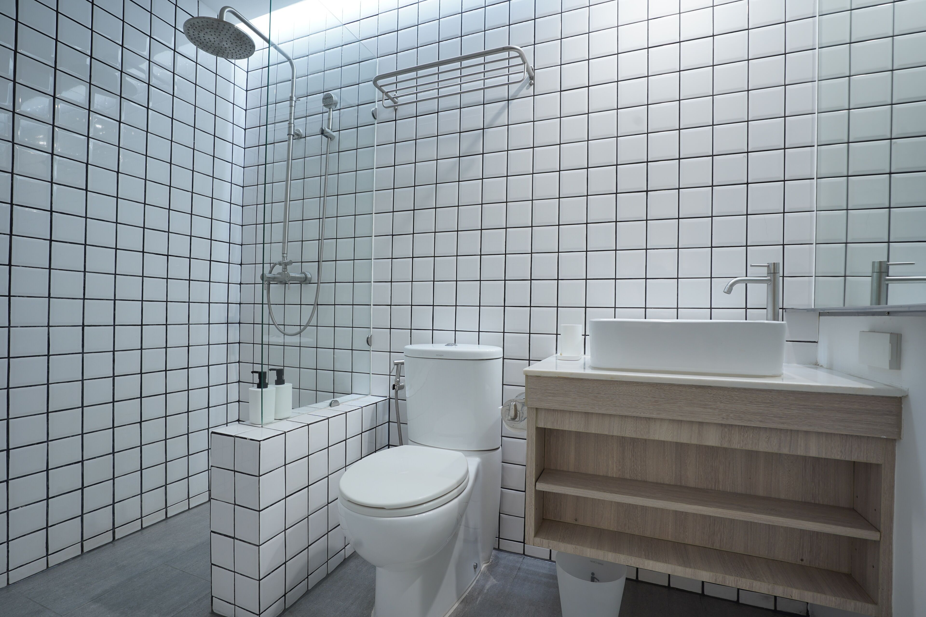 Un baño moderno con azulejos blancos, un inodoro, un lavabo y una ducha.