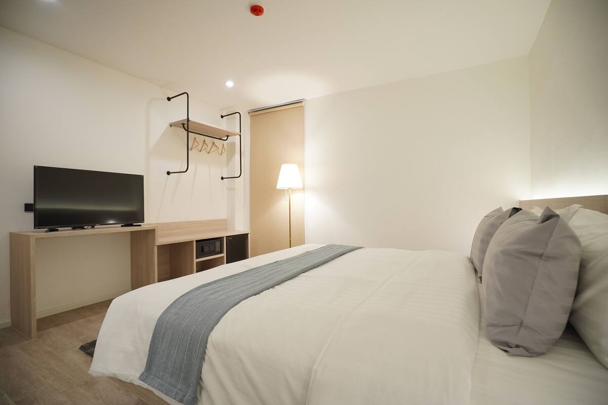 A hotel room with a bed, a TV on a wooden desk, a lamp, and a coat rack.