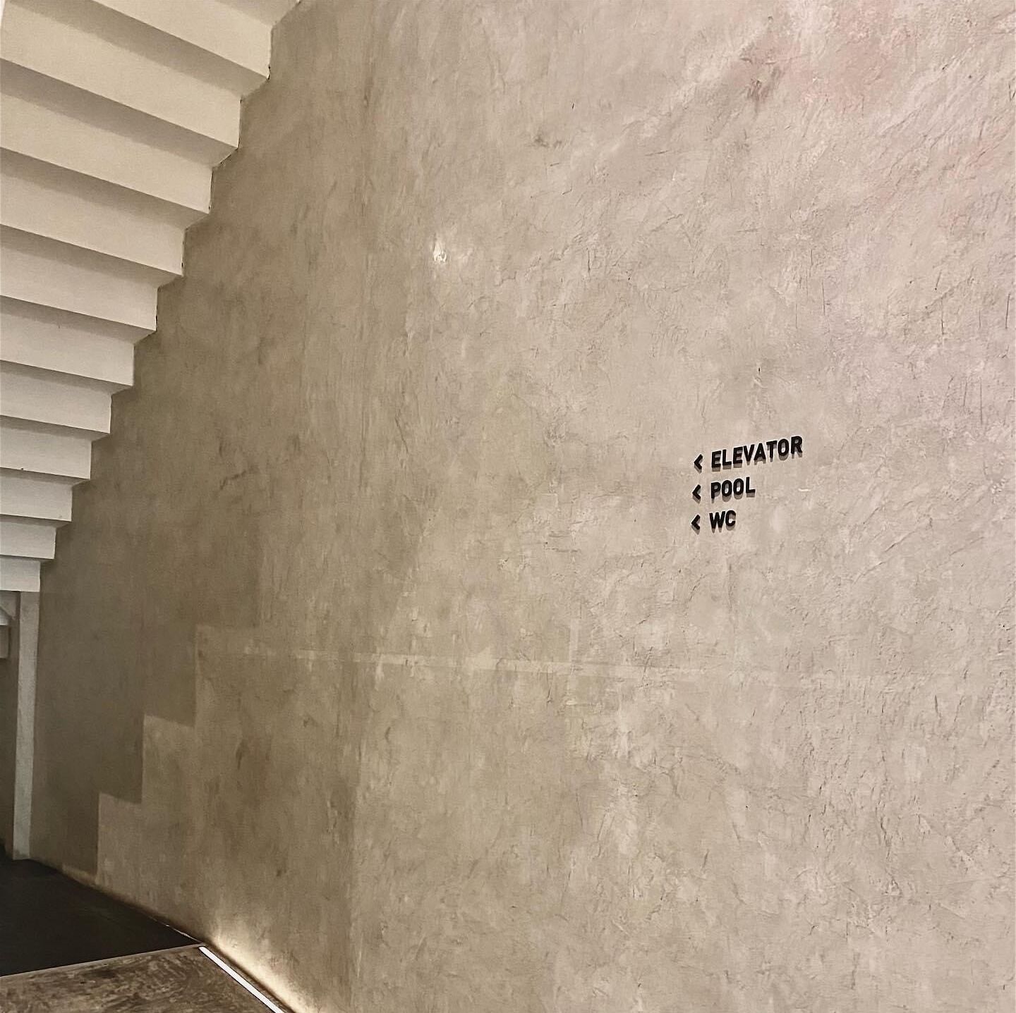 Un mur sur lequel sont affichés des panneaux indiquant la direction de l’ascenseur, de la piscine et des toilettes.