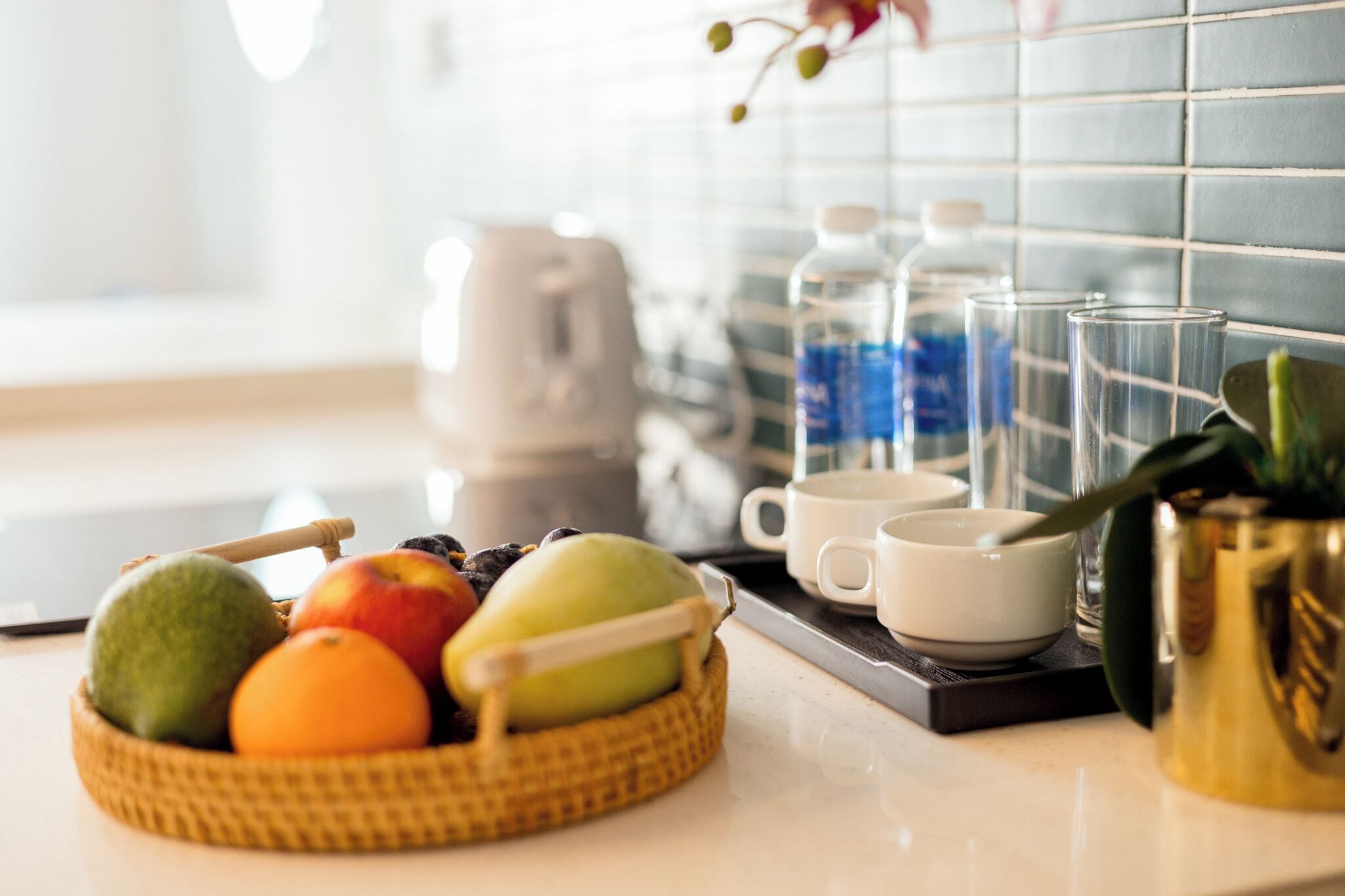 A kitchen counter with a fruit basket, a coffee maker, and a tray with cups and glasses.
