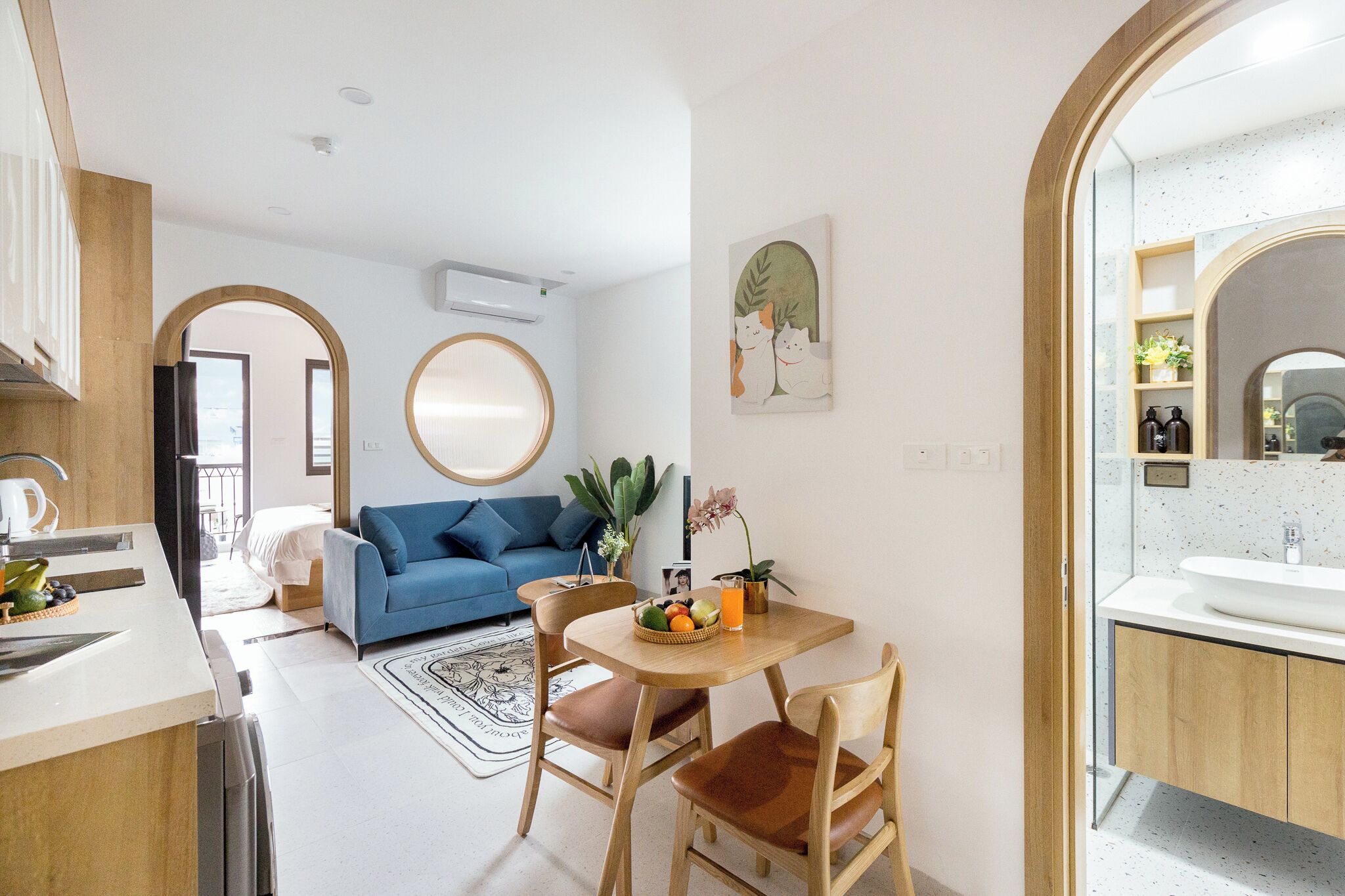 A modern kitchen with a dining area, a blue sofa, and a round mirror.