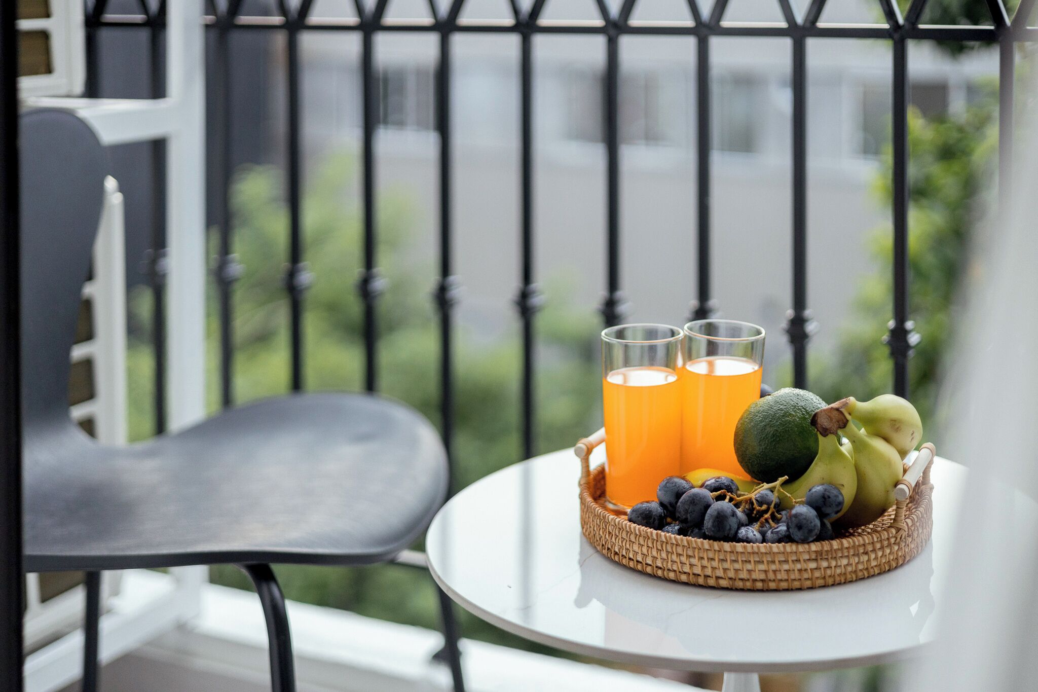 Et bord med en fletkurv fyldt med frugt og to glas appelsinjuice på en balkon.