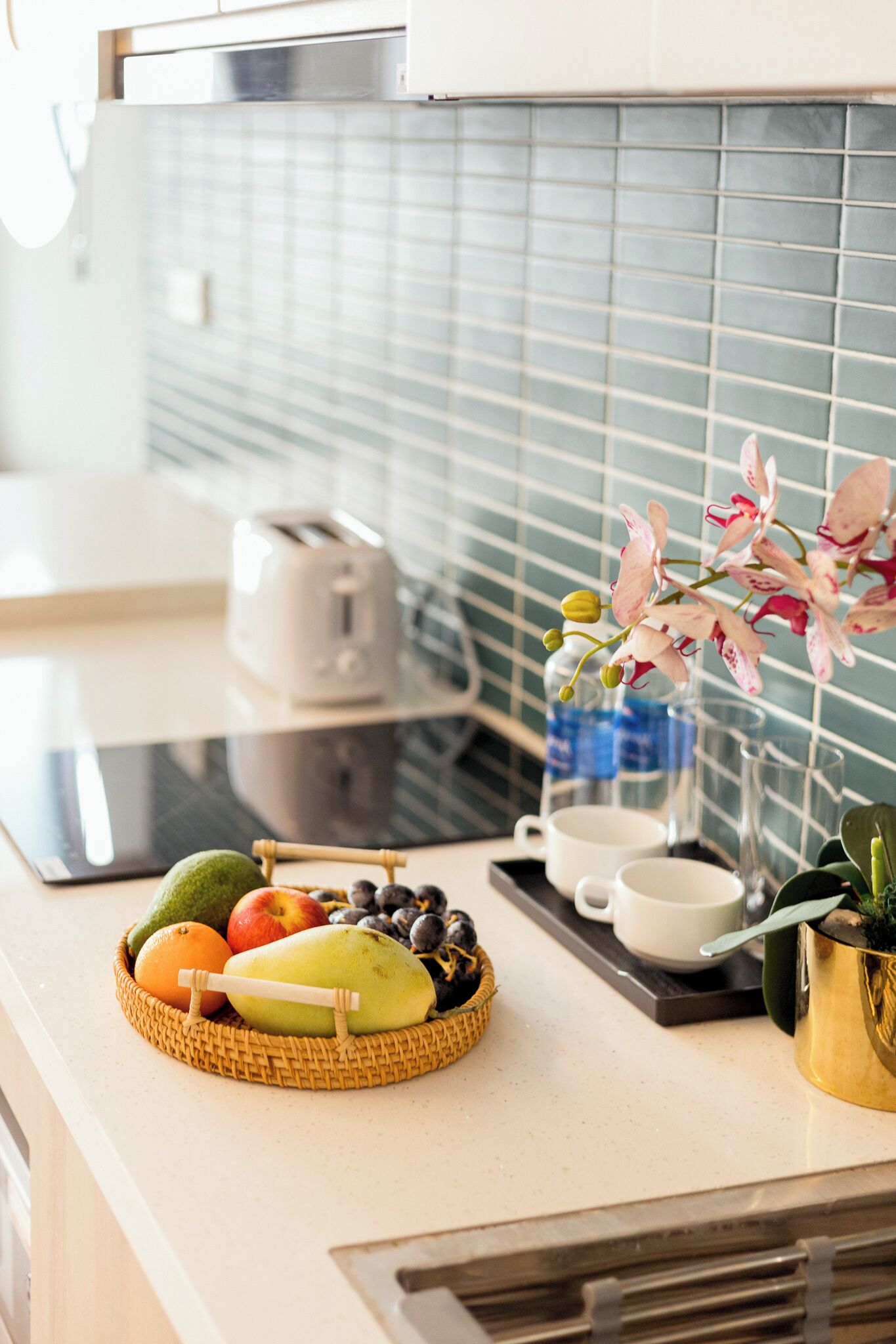 Una encimera de cocina con una cesta de frutas, un tostador y un florero con flores.