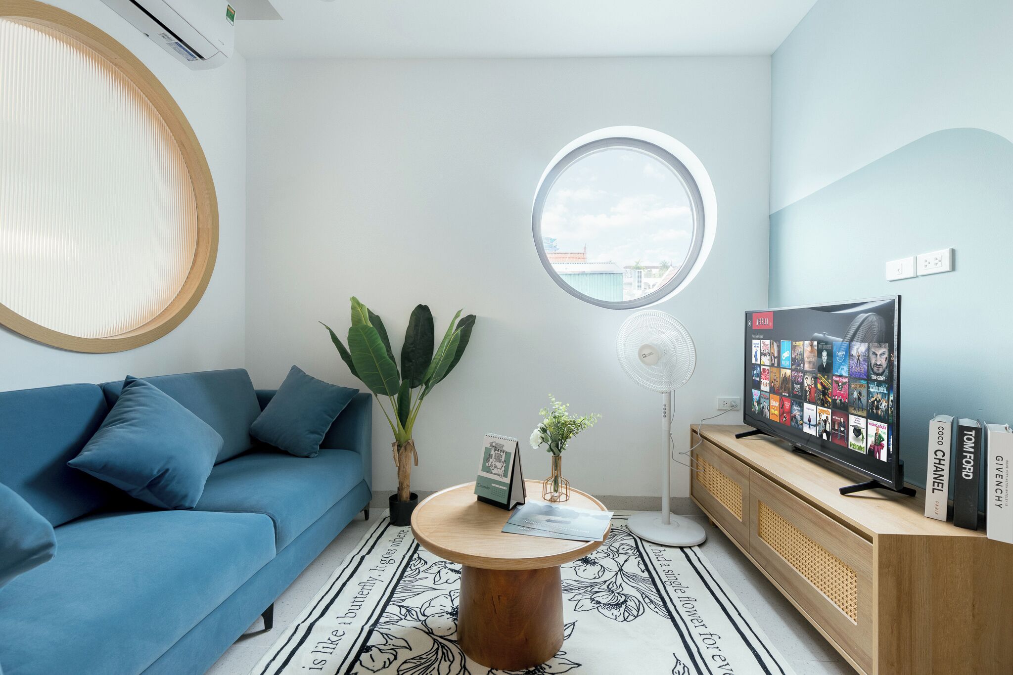A modern living room with a blue sofa, a round coffee table, a TV, and a bookshelf.