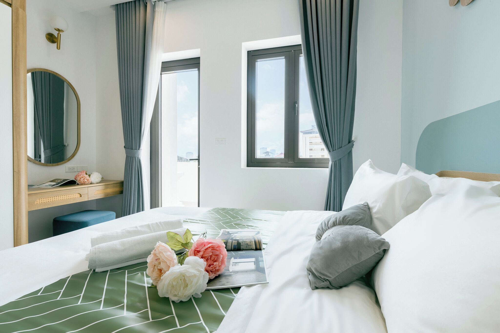 A hotel room with a bed, a desk, a mirror, and a window with curtains.