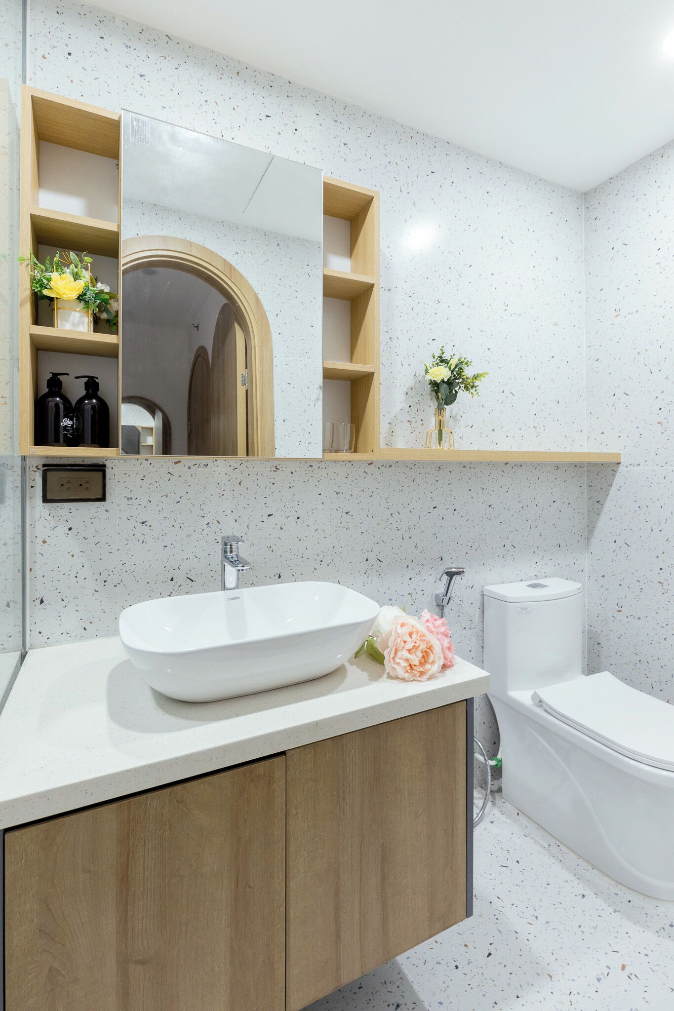 A modern bathroom with a freestanding sink, a toilet, and a bathtub. There are wooden shelves above the sink and a mirror above the bathtub.