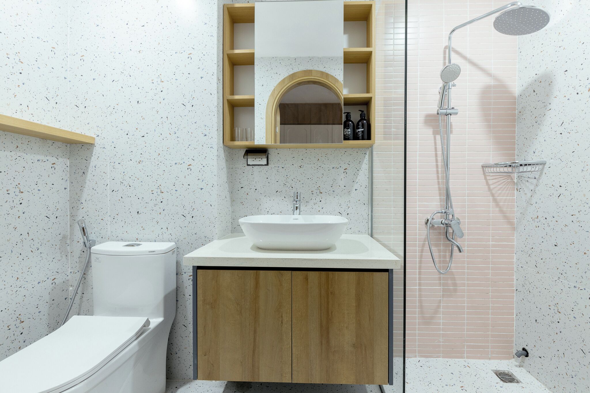 Un bagno con lavandino bianco, mobiletto in legno e doccia con soffione a mano.