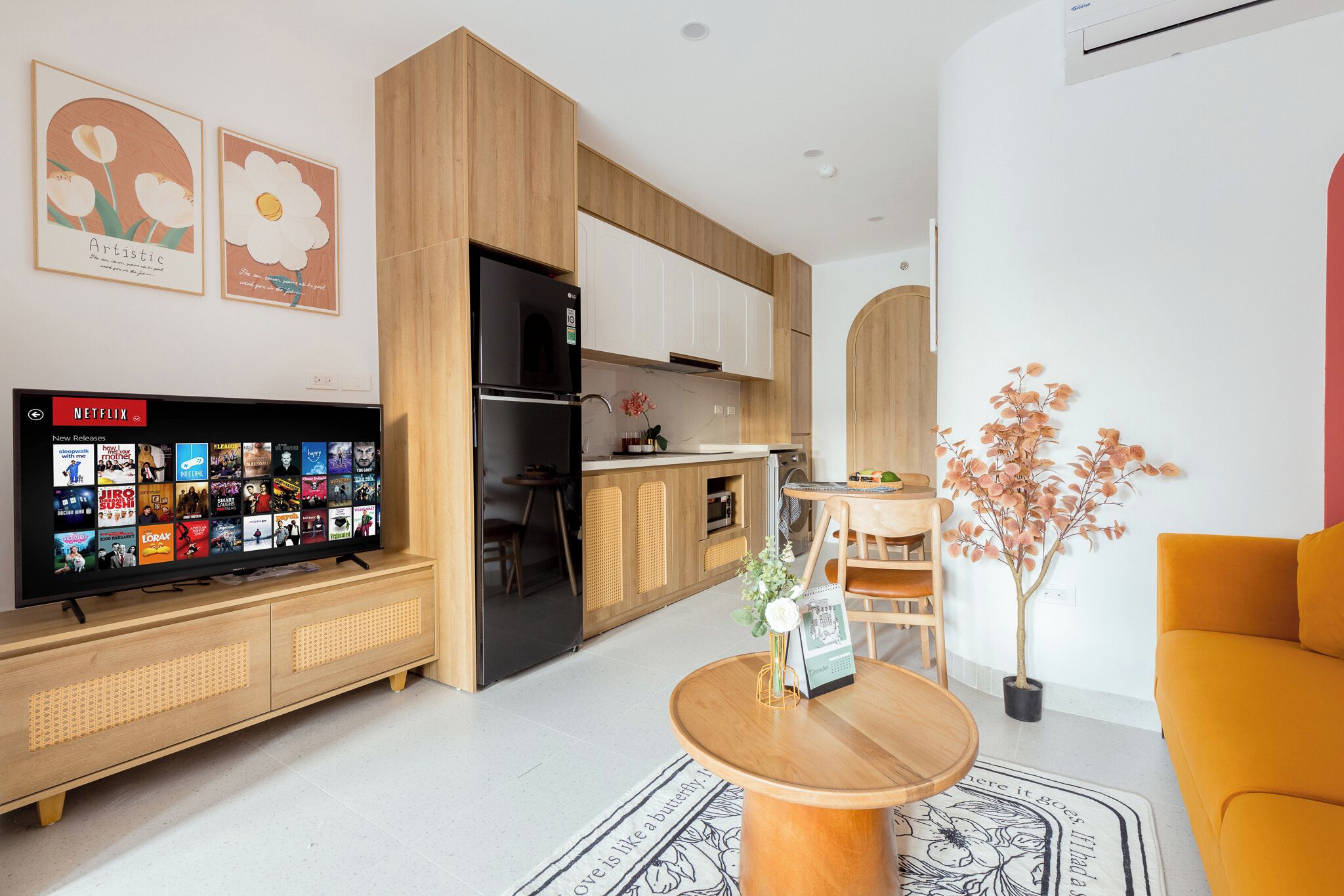 Ett modernt vardagsrum med en platt-TV, träskåp, en matplats och en krukväxt.