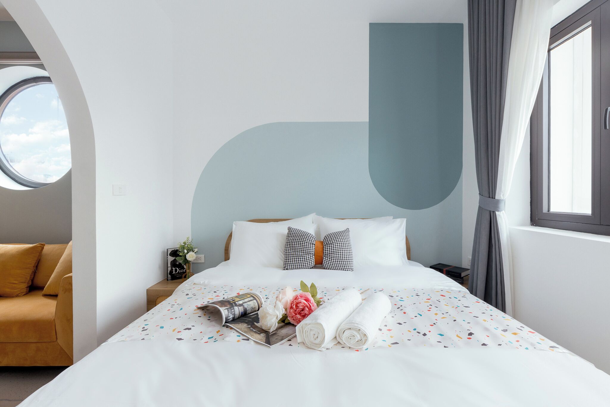 Een keurig opgemaakt bed met een opgerolde handdoek, kussens en een bloemstuk.