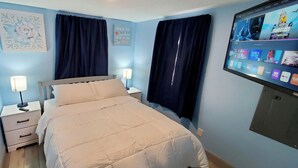 Une chambre à coucher avec un lit, des tables de chevet, une télévision et des rideaux.