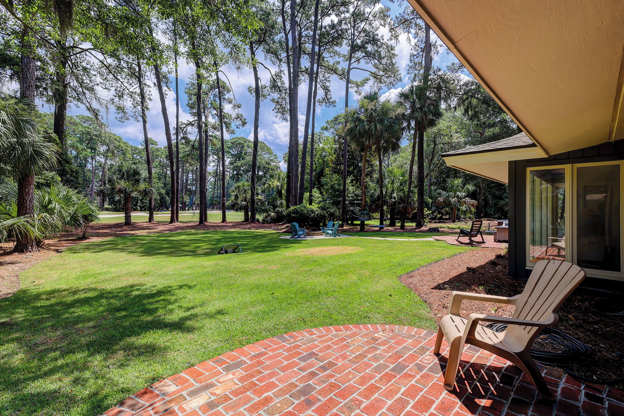 A patio with a brick border, a lawn, and tall trees in the background.