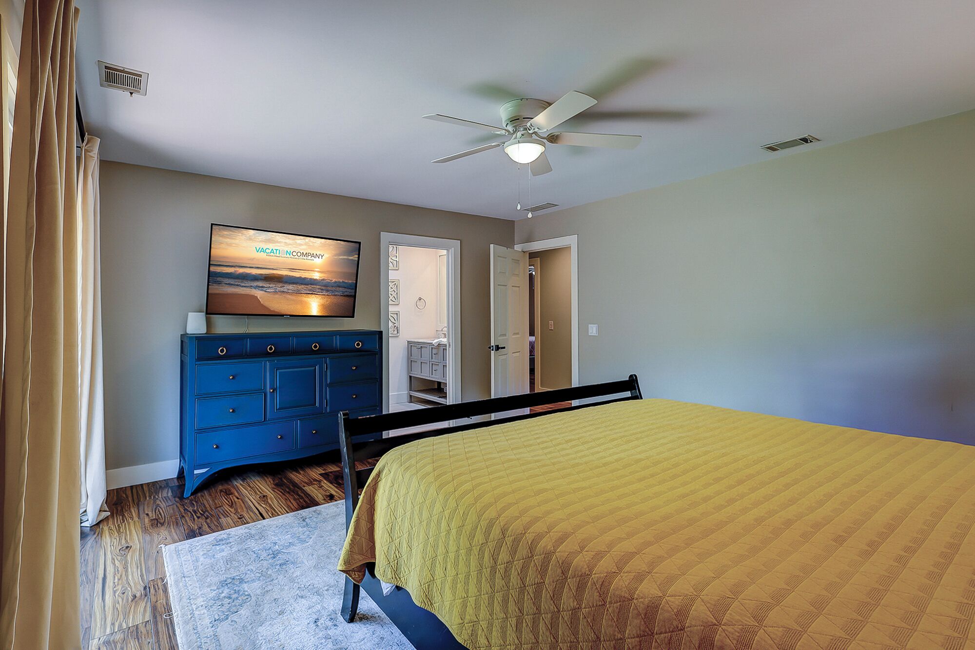 A bedroom with a bed, a dresser, a television, and a ceiling fan.