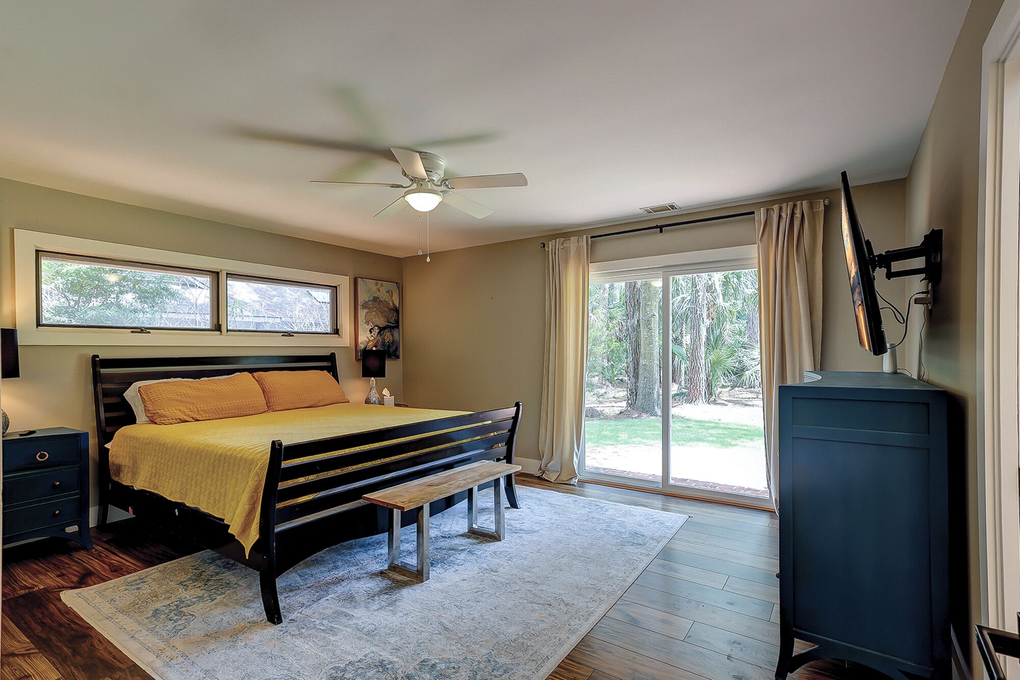Een slaapkamer met een bed, een bureau, een plafondventilator en uitzicht op de omgeving.