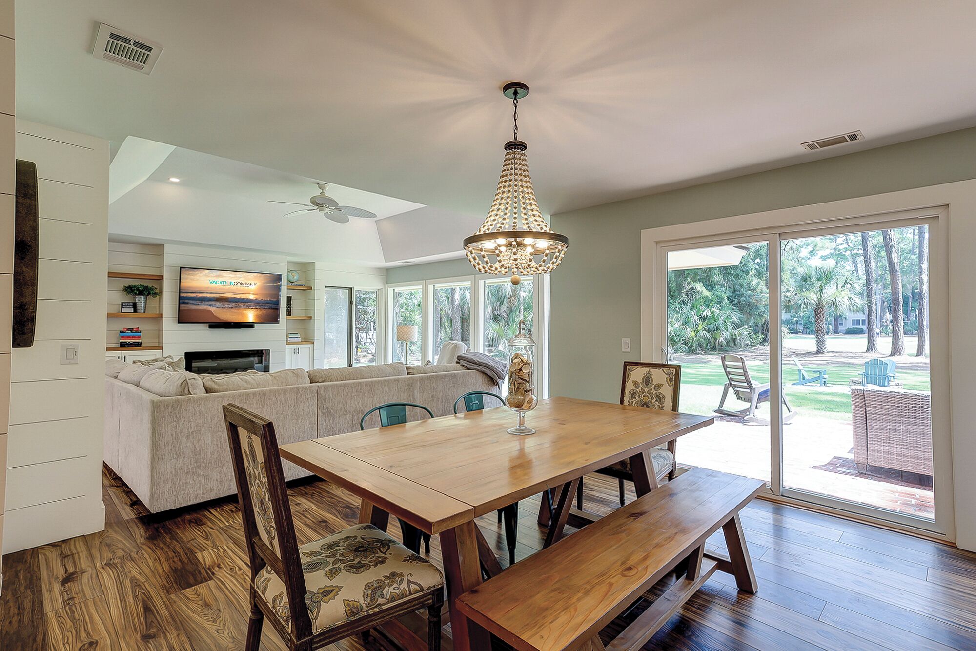 A spacious dining area with a wooden table and benches, a chandelier, and a view of the outdoors through large sliding glass doors.