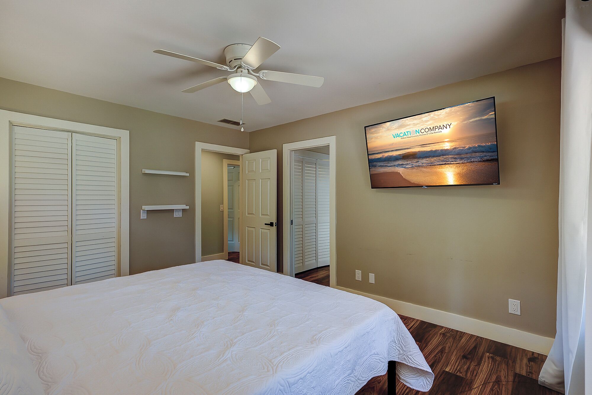 Un dormitorio con cama, ventilador de techo, televisor en la pared y vista a la playa.