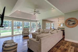 A spacious living room with a large sofa, ottomans, and a dining area with a chandelier.
