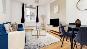 Un salon moderne avec un canapé bleu, une table basse en verre, un téléviseur et un coin repas comprenant des chaises et une table.