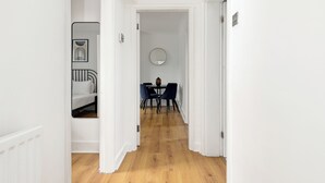 Un couloir qui se termine par un coin repas, avec un grand miroir rond accroché au mur et une table entourée de chaises.