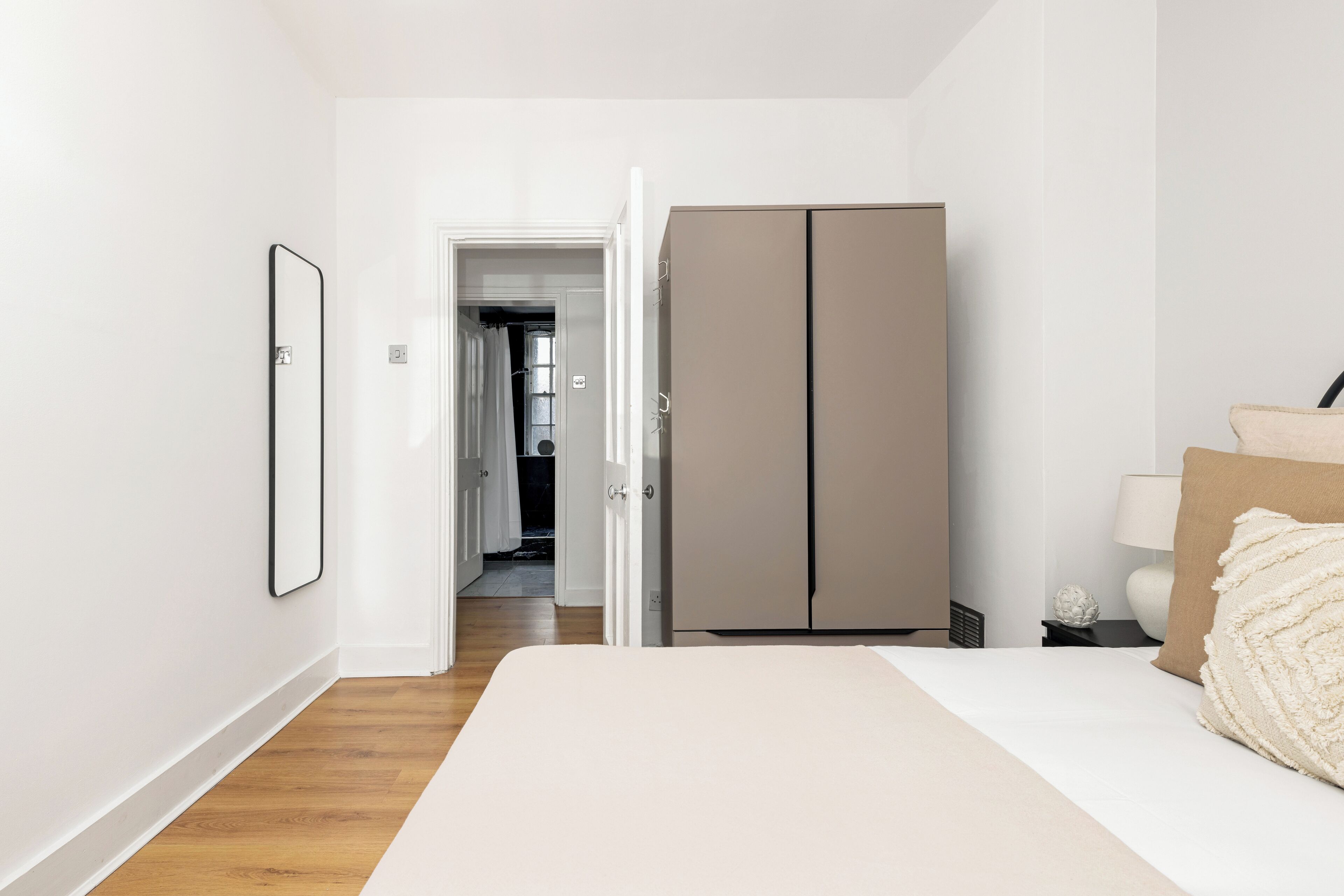 A bedroom with a bed, a wardrobe, a nightstand, and a door leading to another room.