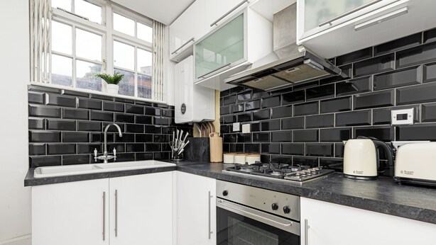 Une cuisine moderne avec des meubles blancs, un dosseret de carreaux noirs, une cuisinière à gaz et un four encastré.