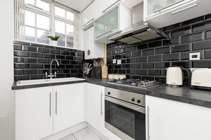 A modern kitchen with white cabinets, a black tiled backsplash, a gas stove, and a built-in oven.