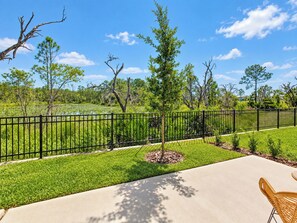 A patio area with a concrete floor, a black metal fence, and a grassy field with trees in the background.