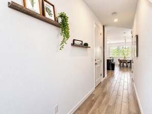 Um corredor com piso de madeira, paredes brancas e porta que dá para uma sala de jantar.
