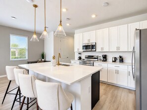 A modern kitchen with white cabinetry, stainless steel appliances, and a central island with bar stools.