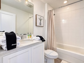A bathroom with a white sink, toilet, and bathtub. There are towels and toiletries on the counter.