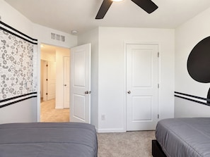 A bedroom with two beds, a ceiling fan, and a door leading to another room.