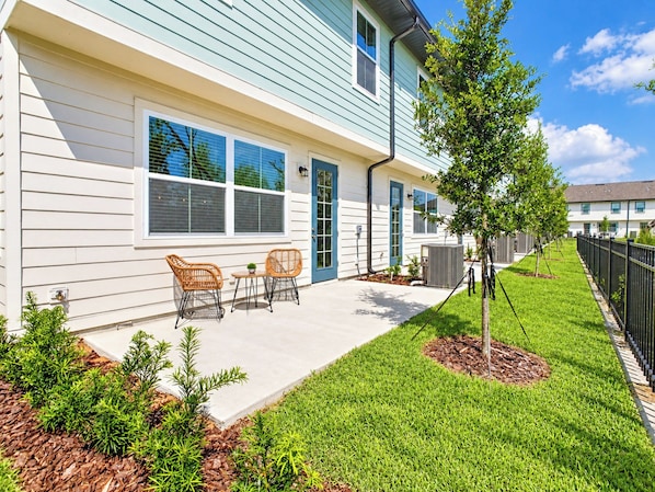 A residential building with a covered patio area, outdoor seating, and a well-maintained lawn.