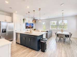 A modern kitchen with a central island, stainless steel appliances, pendant lighting, and a dining area with a table and chairs.